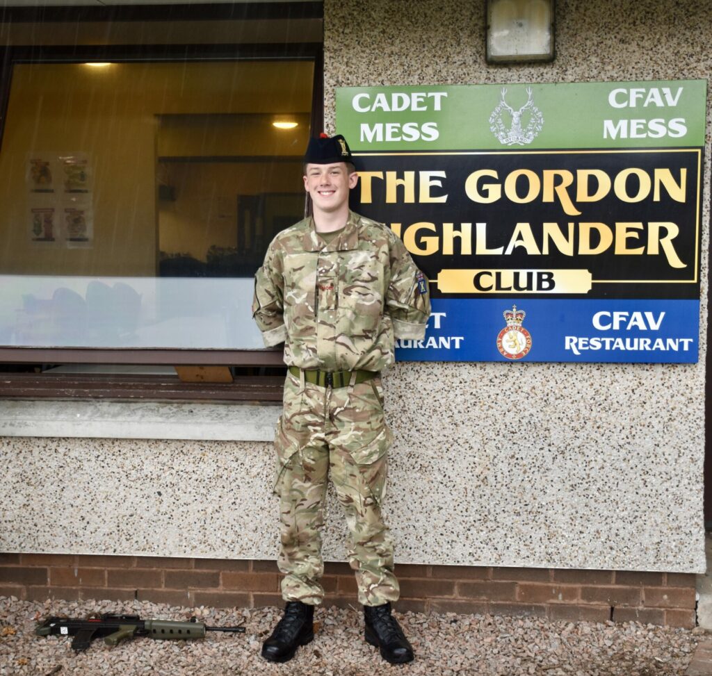 Cadet standing next to sign with weapon at his feet