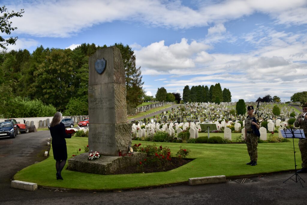 Woman laying wreath at memorial with two musicians