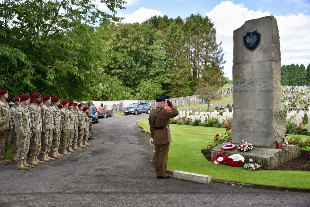 Group of cadets standing next to man saluting at memorial