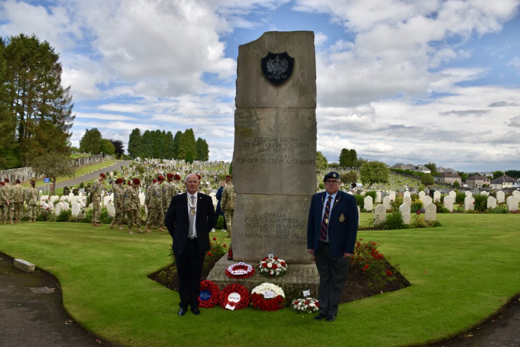 Two men standing next memorial with cadets and war graves behind