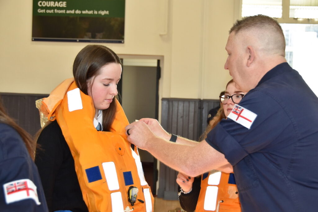 A sailor adjusts a visitors life vest.