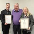 Three people holding two framed certificates.
