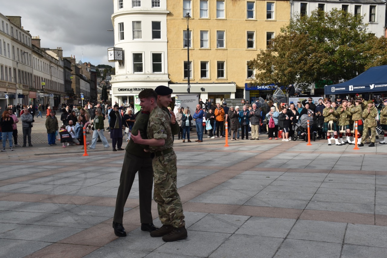Two cadets shaking hands and hugging in front of the crowd.