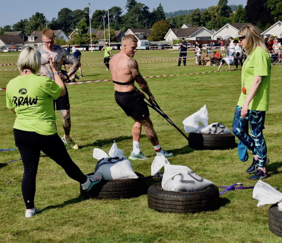A man dragging a weighted tyre on grass.