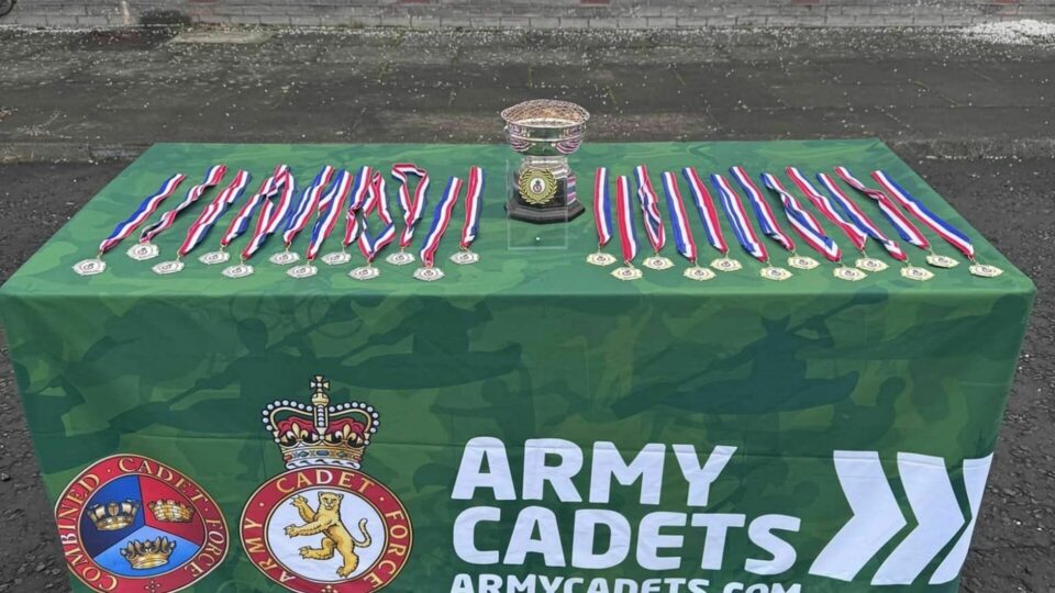 Drill competition medals and trophies on a table with Army Cadets branding.