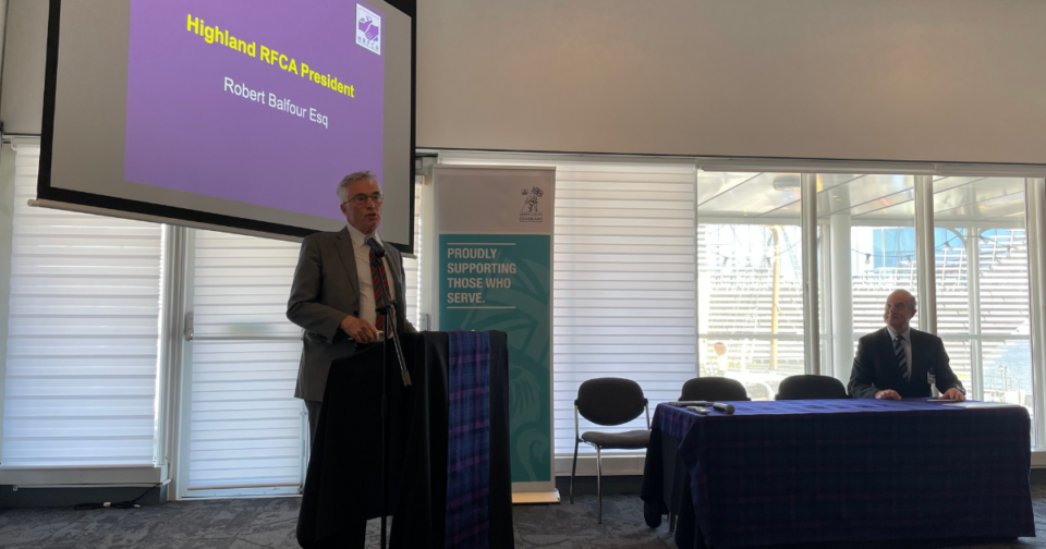 A man standing at a lectern and a man sitting at a table.