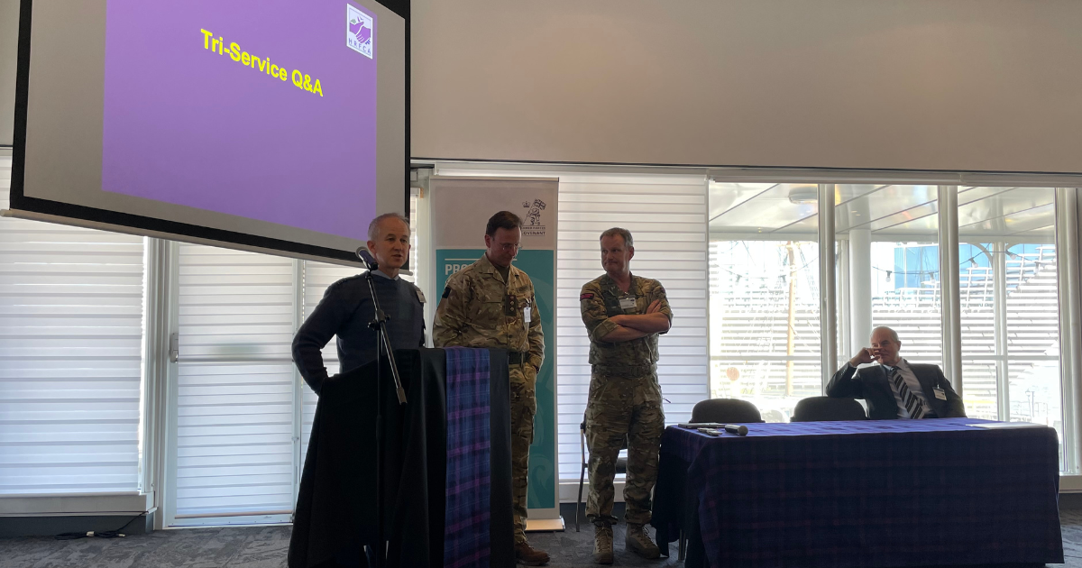 Three people standing at a lectern and one person sitting at a table.