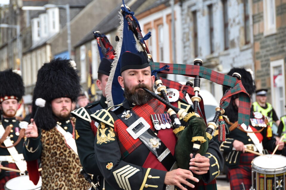A piper marches through Lochgilphead alongside fellow band members.